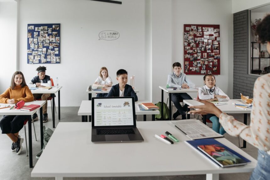 Teacher's desk with a laptop showing an AI lesson-planning assistant beside differentiated printed worksheets