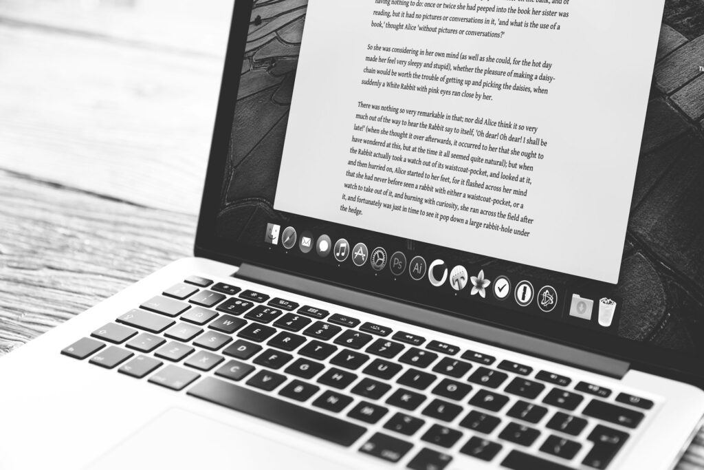 Laptop showing a writer's draft with AI feedback comments beside a hand-edited printout