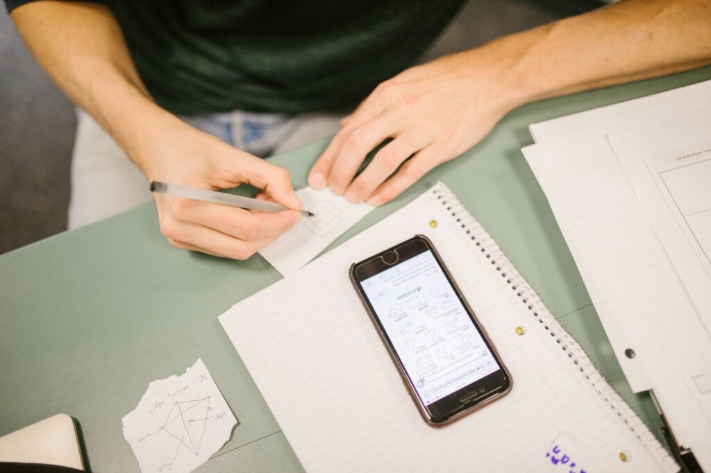 Student using AI exam notes tools on a laptop and phone two weeks before an exam, with condensed one-page revision sheets on the desk, illustrating the best AI for making notes for exams.